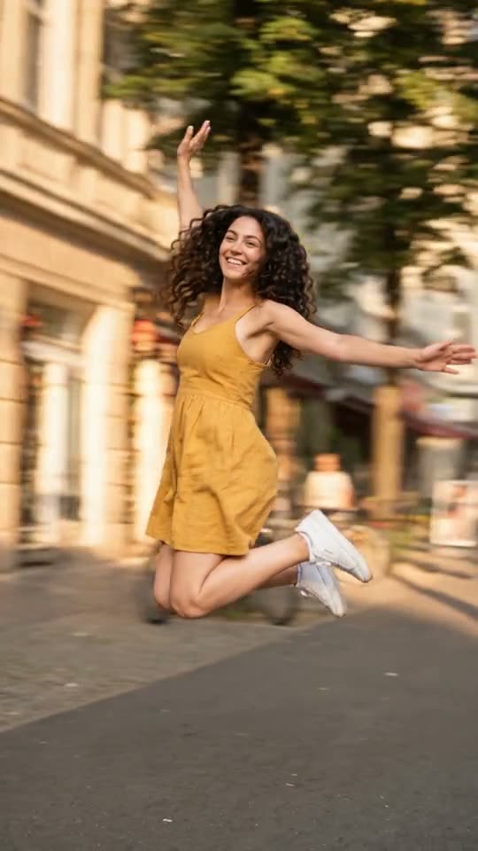 Woman in a yellow sundress frozen mid-jump on a sunny city sidewalk